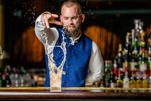Ein Barkeeper hinter einem Cocktailglas mit einer in der Bewegung eingefangenen Flüssigkeitsfontäne