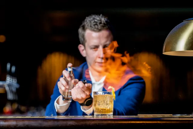 Ein Barkeeper inszeniert einen Cocktail mit einer Flamme über dem Glas
