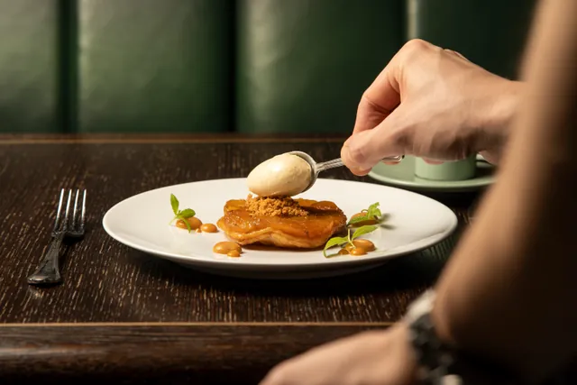 Eine Hand setzt eine Kugel Eis auf ein angerichtetes Dessert